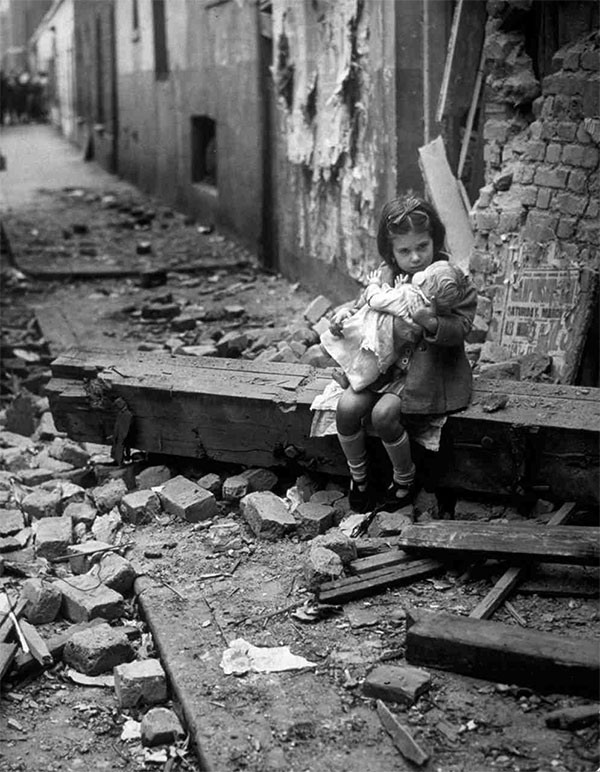 An English girl comforts her doll in the rubble of her bomb-damaged home. 1940.
